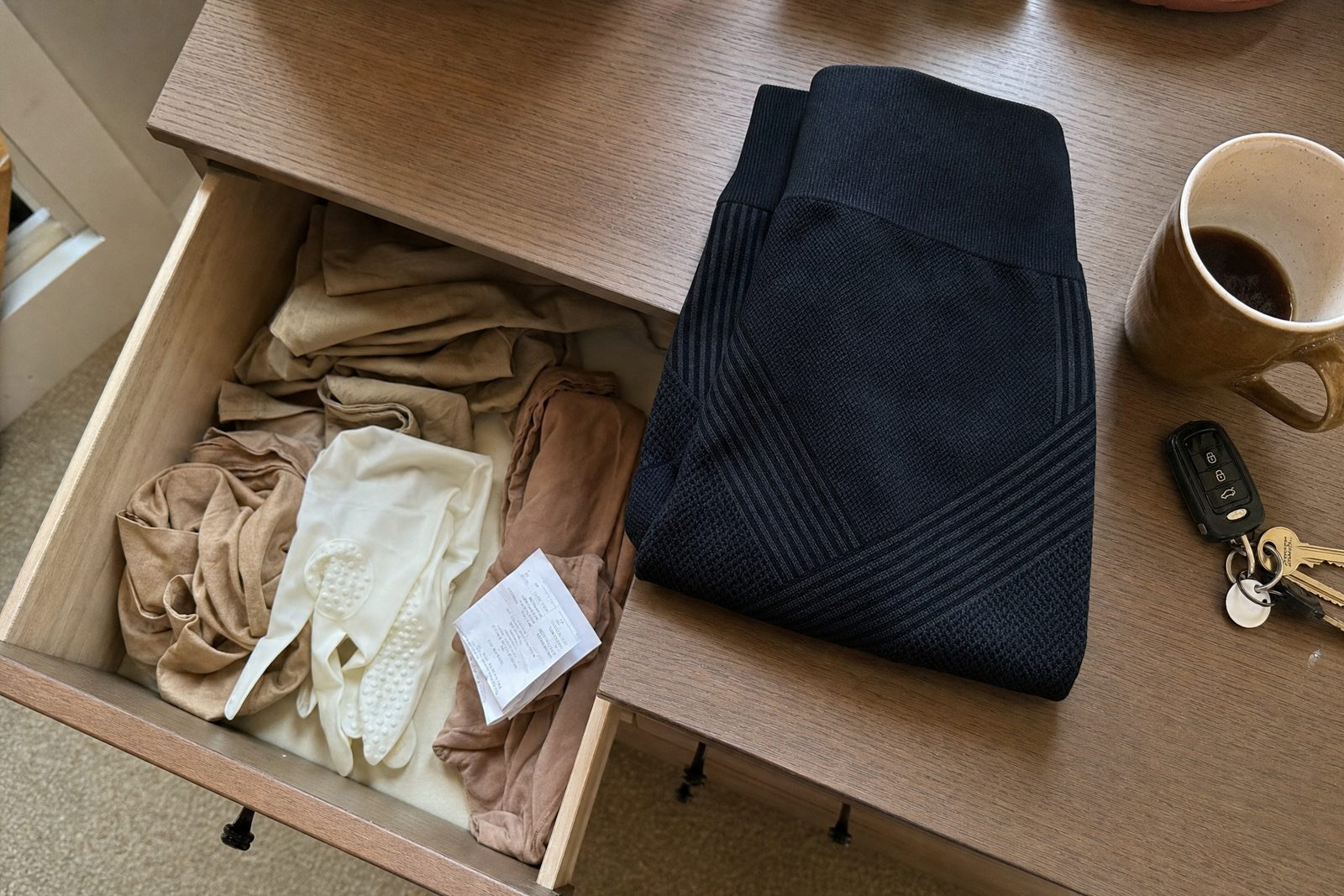 An open dresser drawer of unworn beige medical stockings, with black compression leggings folded on top